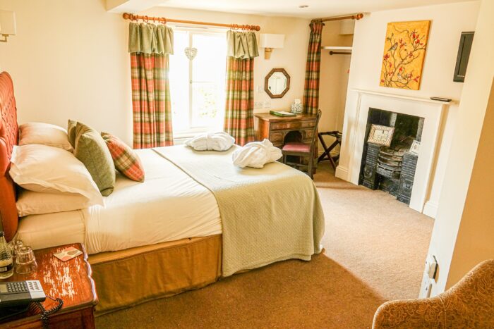 Willow Room at The Oak Tree featuring bed with window draped in plaid curtains, a fire is across from the bed.